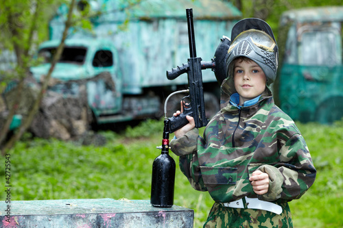 Boy in the camouflage suit holds a paintball gun barrel up