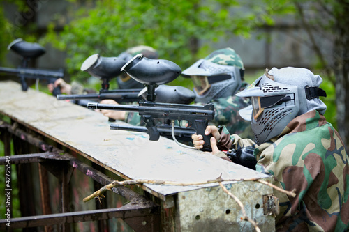 Four paintball players in camouflage and protective masks aims