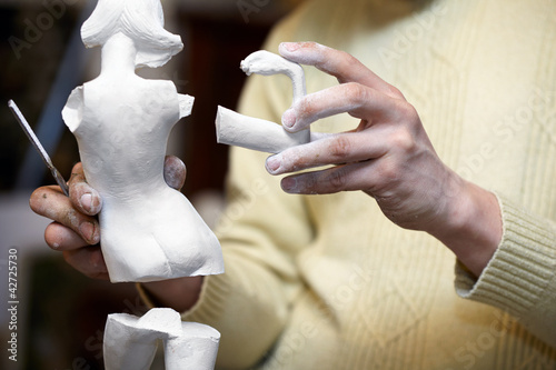 Obraz na plátně Hands of sculptor hold parts of plaster statuette.