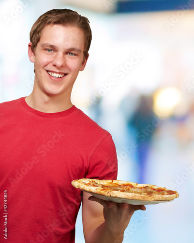 young man holding pizza against a abstract background