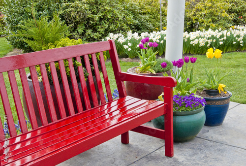 Red garden bench on patio with pots of spring flowers