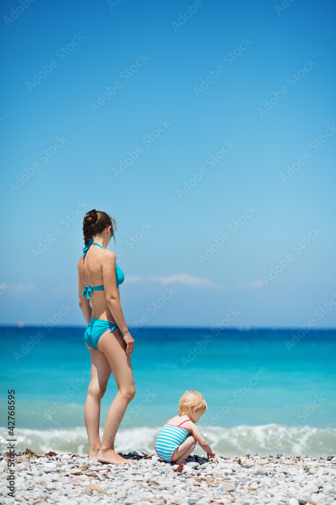 Mother and baby on sea shore. Rear view