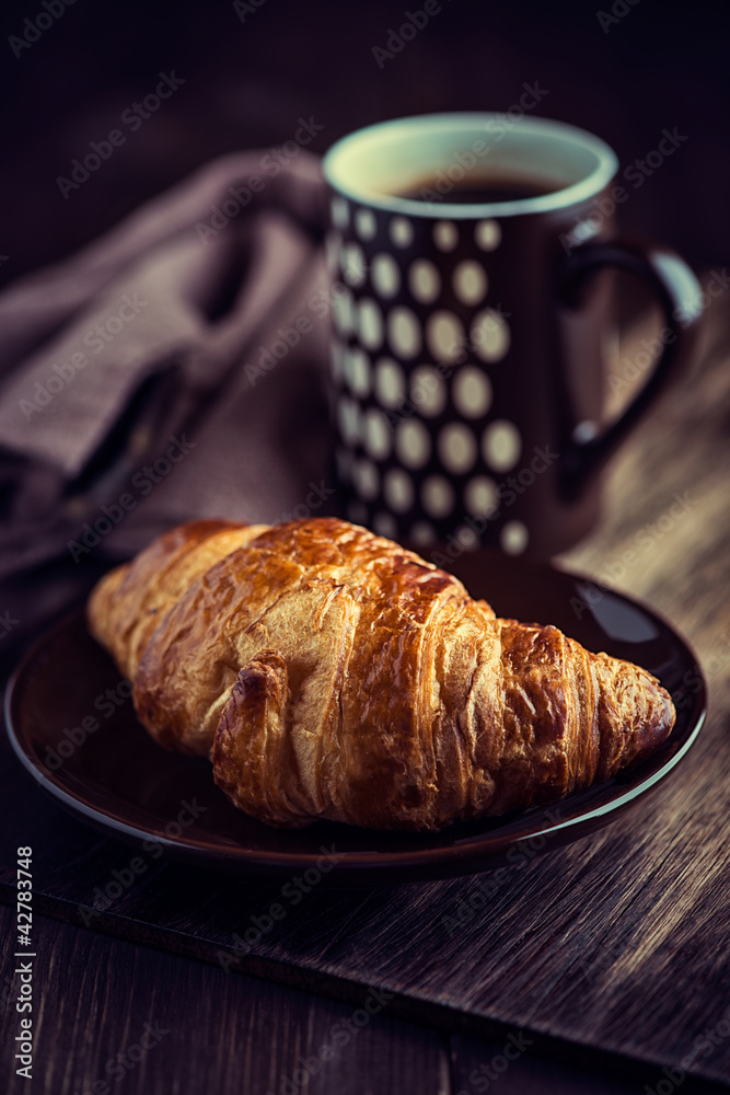Croissant and a mug of coffee on dark wooden background