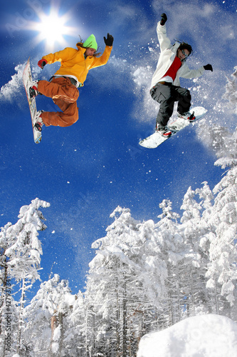 Snowboarders jumping against blue sky