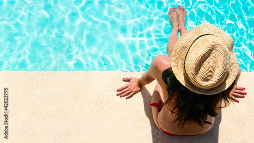 Woman sitting in a swimming pool with a sunhat