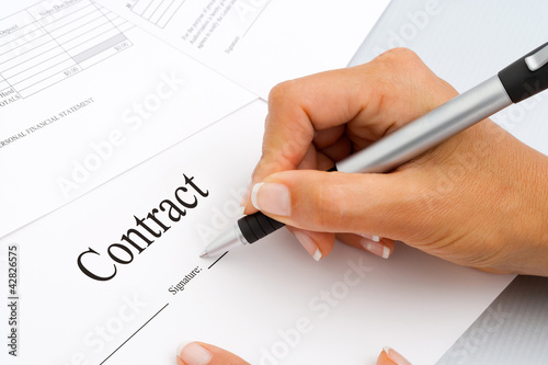 Close up of hand signing contract documents.