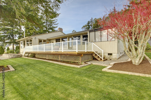 Beige one story house with deck and grass during spring.