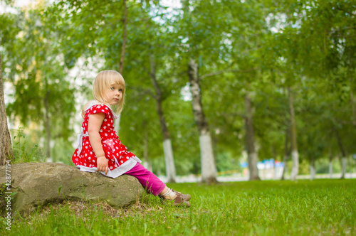 Adorbale girl in beautiful dress sit on rock in park