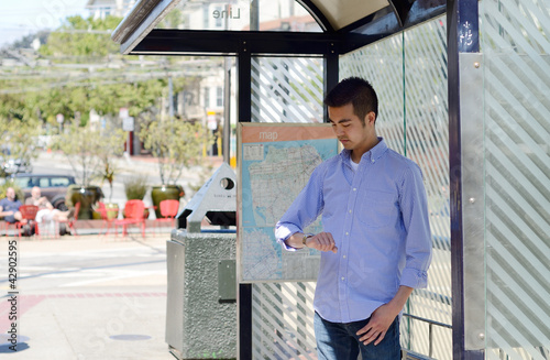 man at a bus stop checking his watch as he waits