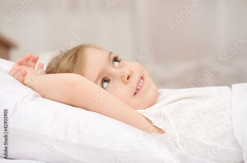 The little girl lies in a bed with the pensive