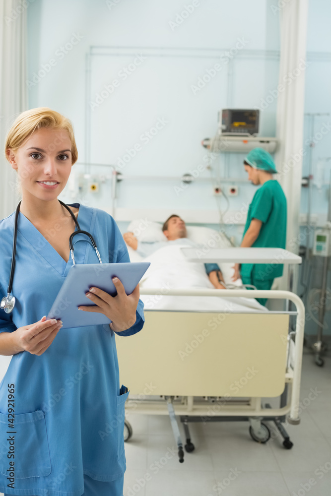 Blonde nurse holding a tablet computer next to a bed