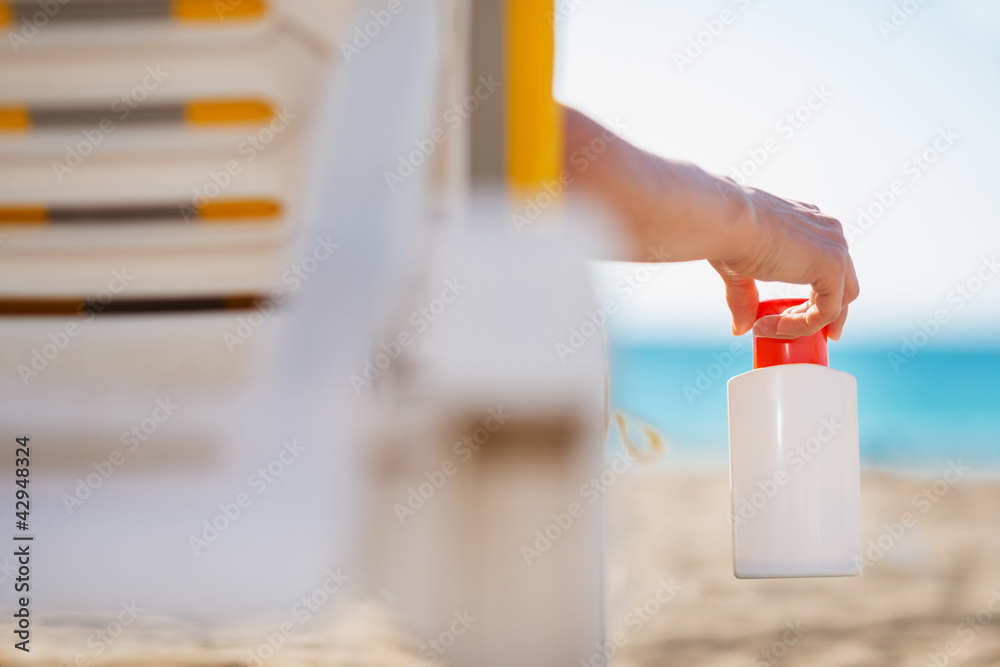 Closeup on bottle of sun screen in hand of female laying on sunb Closeup on bottle of sun screen in hand of female laying on sunb