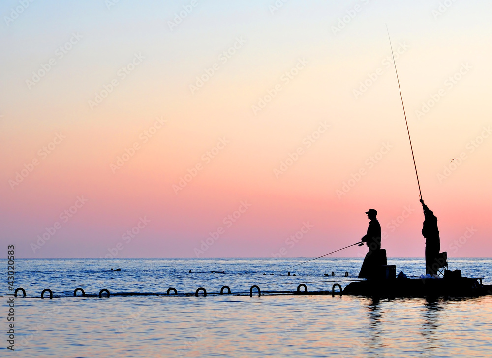 Silhouettes of two fishermen in the sea at sunset Silhouettes of two fishermen in the sea at sunset