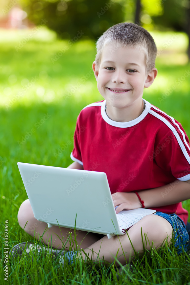 boy sitting with a laptop on the grass boy sitting with a laptop on the grass