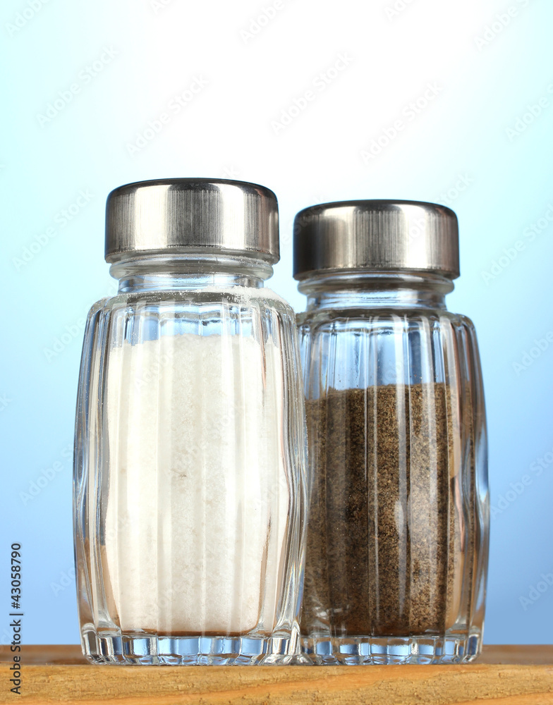 Salt and pepper mills, on wooden table on blue background Salt and pepper mills, on wooden table on blue background