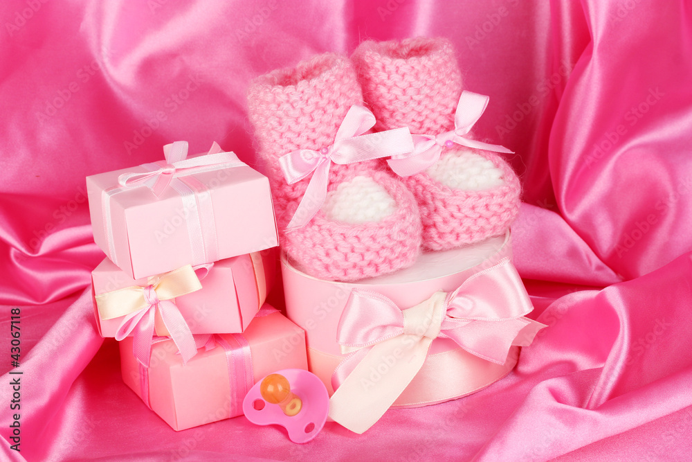 pink baby boots, pacifier, gifts on silk background. pink baby boots, pacifier, gifts on silk background.