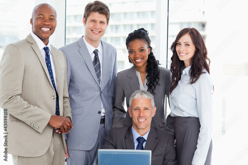 Mature manager smiling with a computer among his team Mature manager smiling with a computer among his team