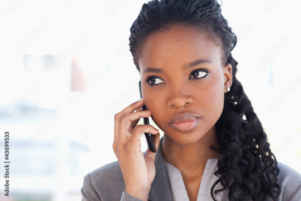 Young earnest employee talking on the phone in front of a bright Young earnest employee talking on the phone in front of a bright