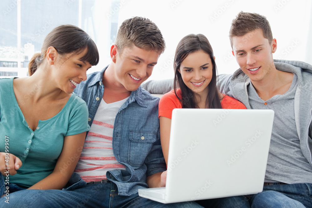 A smiling group of friends sitting around a laptop A smiling group of friends sitting around a laptop
