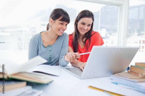 Two girls smiling as they use the laptop as one girl points at s