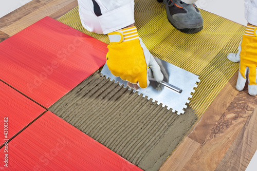 worker apply ceramic tiles on wooden floor mesh trowel