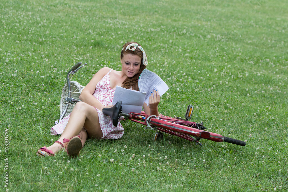 Beautiful girl with her bicycle, in a garden while is reading