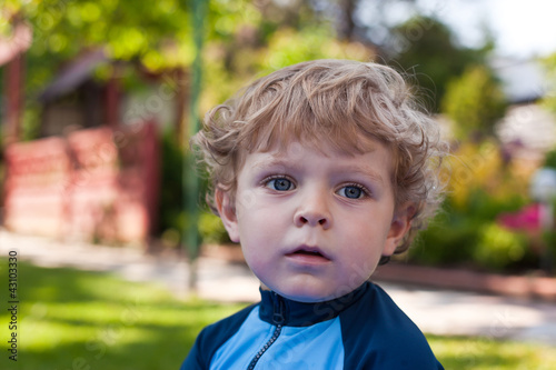 cute boy with blond hairs and blue eyes in summer garden