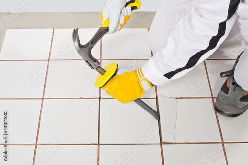 Worker with hammer removes old white tiles from floor