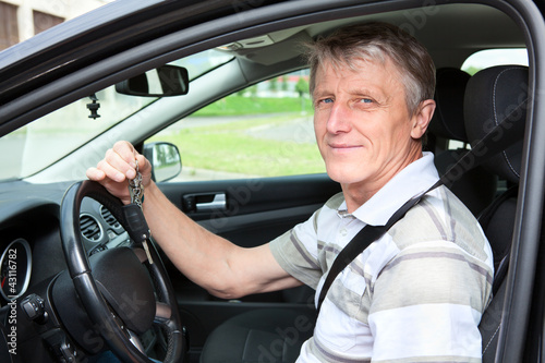 Happy mature driver with car key sitting in own car