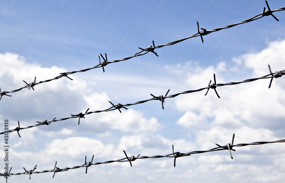 Barbed wire against blue sky with clouds Barbed wire against blue sky with clouds