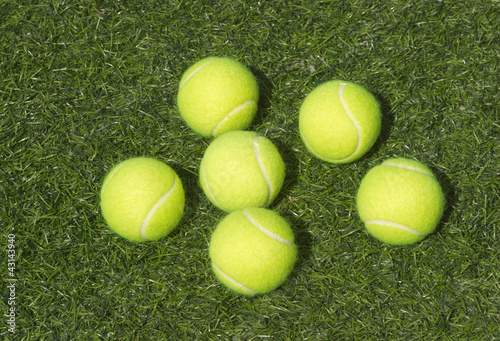 SIx yellow tennis balls lays on green synthetic court grass © DyMaxFoto