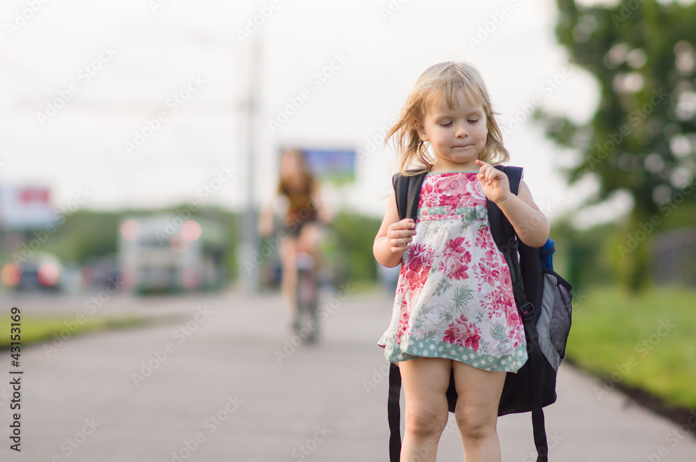 Adorable girl with huge backpack and toy shovel stay on road in