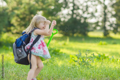 Adorable girl with huge backpack and toy shovel walking in park