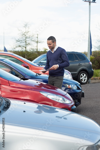 Man looking at a car while holding a file