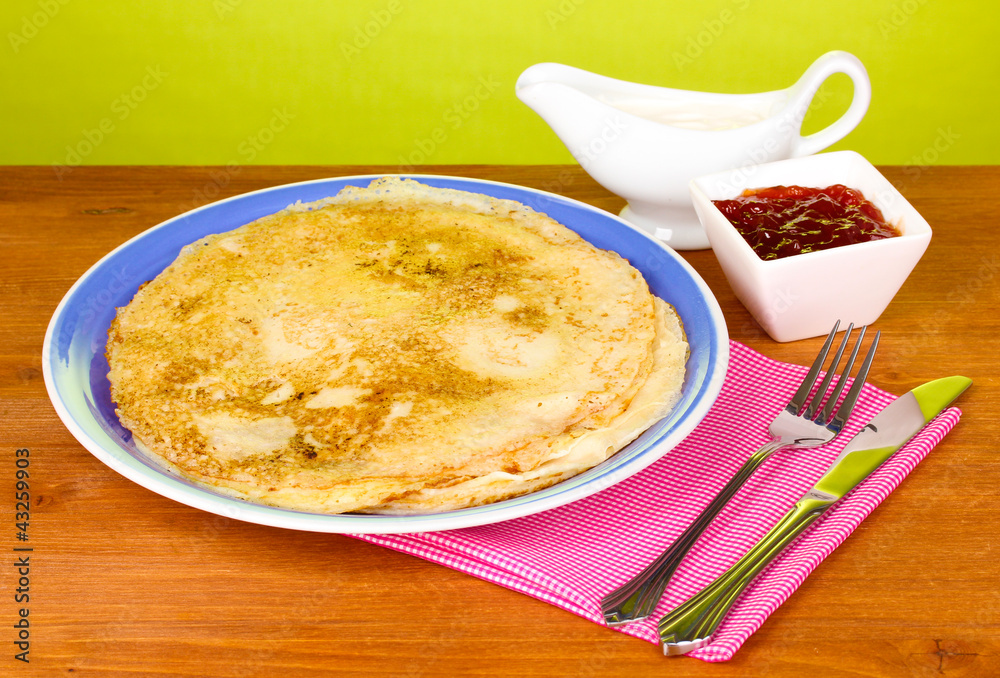 Stack of tasty pancakes on wooden table on green background Stack of tasty pancakes on wooden table on green background