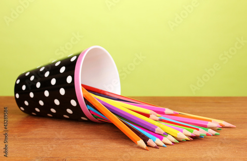 Color pencils in glass on wooden table on green background