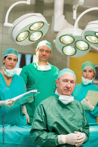 Surgeon sitting while crossing his hands with a team behind him