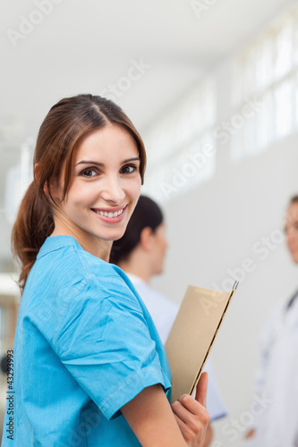 Nurse smiling while holding files and standing with a doctor and