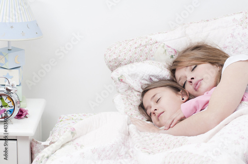 Hispanic mother and daughter sleeping together in bed