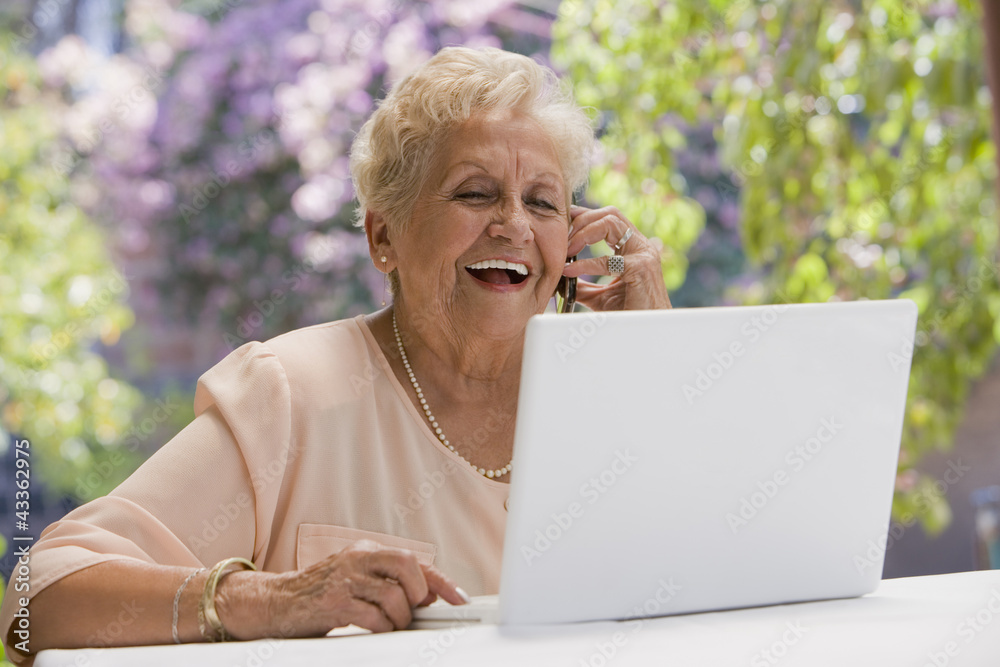 Senior Hispanic woman using laptop and talking on cell phone Senior Hispanic woman using laptop and talking on cell phone