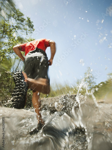 Mixed race man running through stream