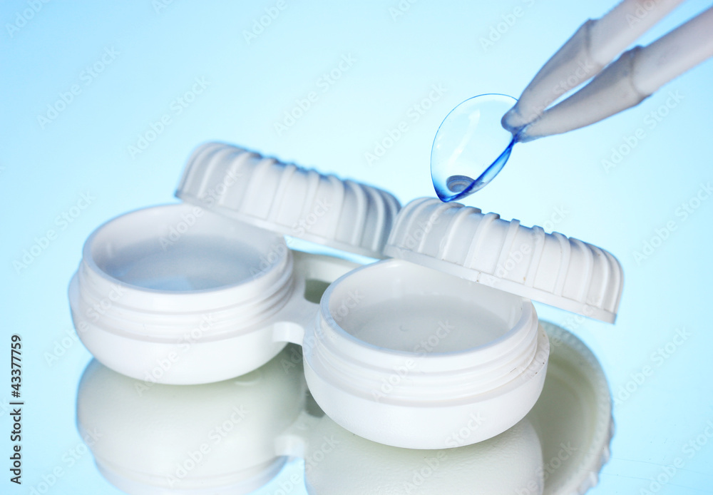 contact lenses in containers and tweezers on blue background