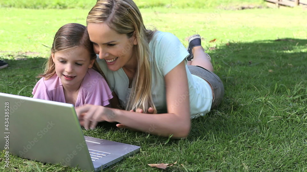Mother and his daughter using a laptop in a park Mother and his daughter using a laptop in a park
