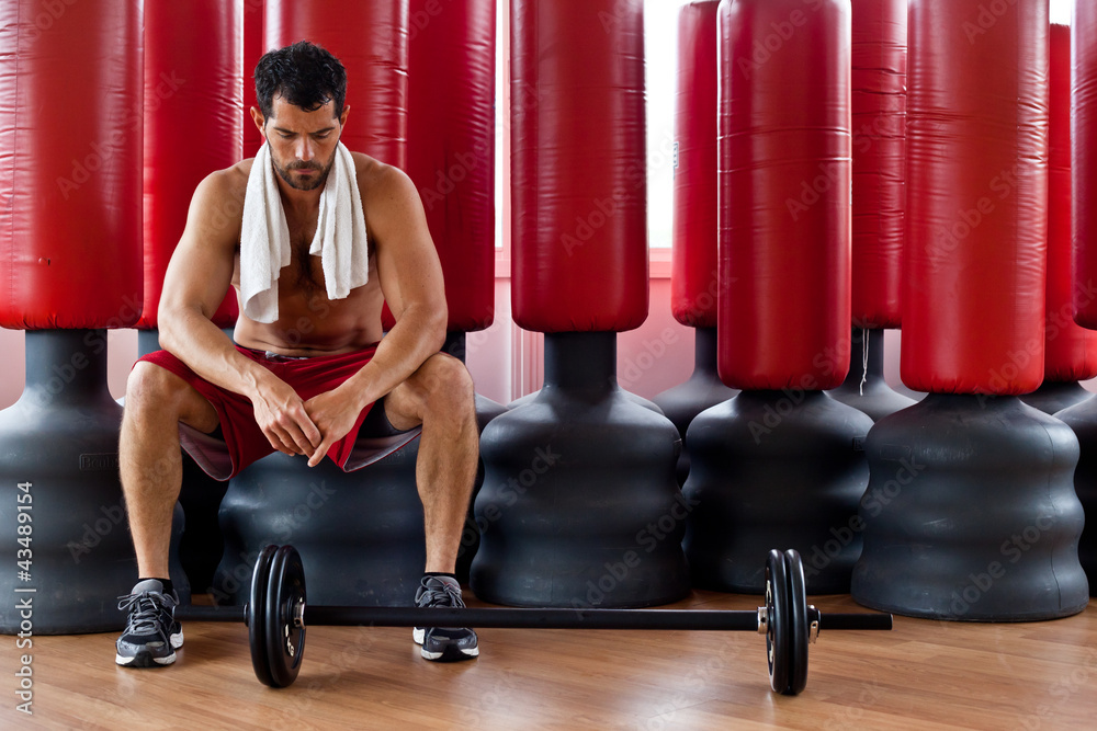 Handsome muscular man sitting in front of red punching bags.
