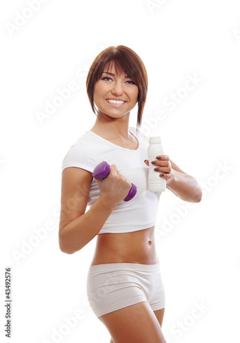 A young and fit brunette woman holding a dumbbell and a bottle