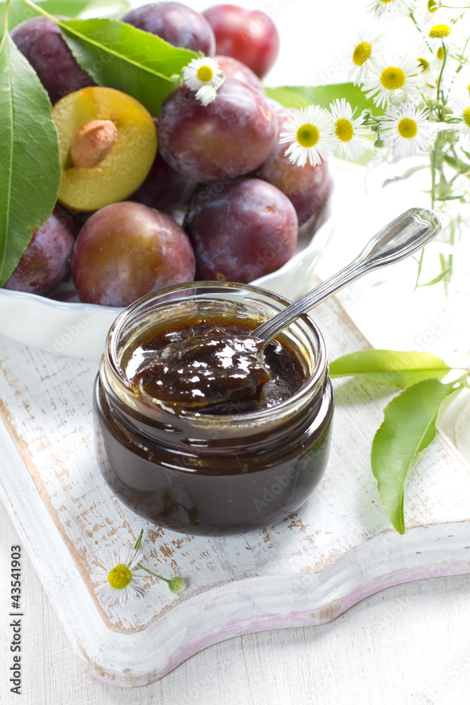 Plum jam in a glass jar and fresh fruits with leaves