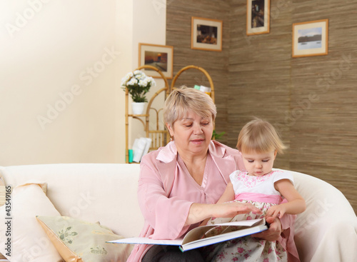 The grandmother reads to the grand daughter the book on a sofa