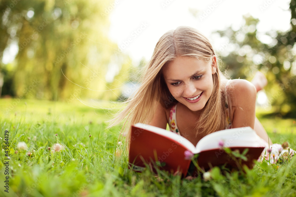 Young woman reading book at park lying down on grass Young woman reading book at park lying down on grass