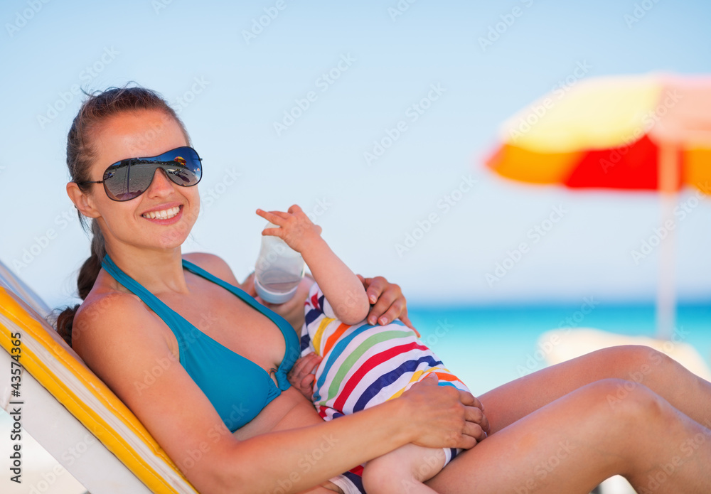 Mother laying on sun bed and holding baby drinking water Mother laying on sun bed and holding baby drinking water
