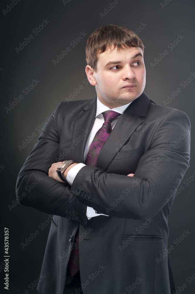 A young man stands with his arms folded across his chest. On a d A young man stands with his arms folded across his chest. On a d